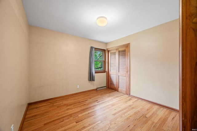 unfurnished bedroom featuring a closet, baseboards, baseboard heating, and light wood-type flooring