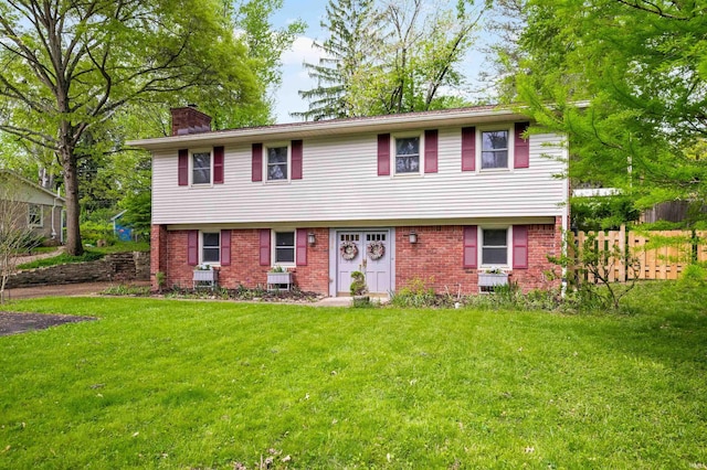 colonial home featuring brick siding, a front lawn, fence, and a chimney