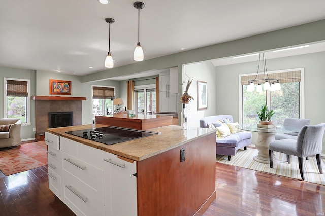 kitchen with dark wood-style flooring, a tiled fireplace, black electric cooktop, open floor plan, and white cabinetry