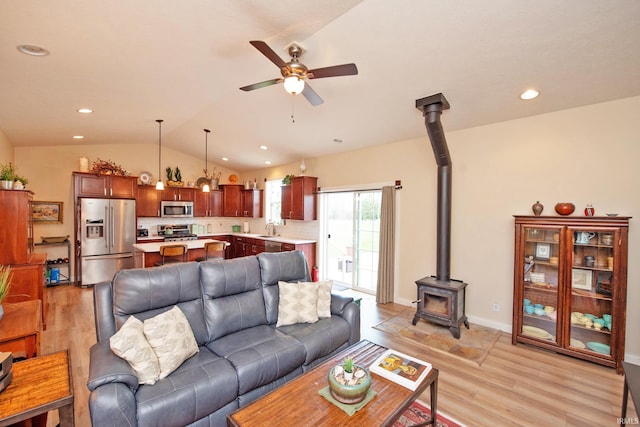 living area featuring a wood stove, light wood-style floors, a ceiling fan, recessed lighting, and lofted ceiling
