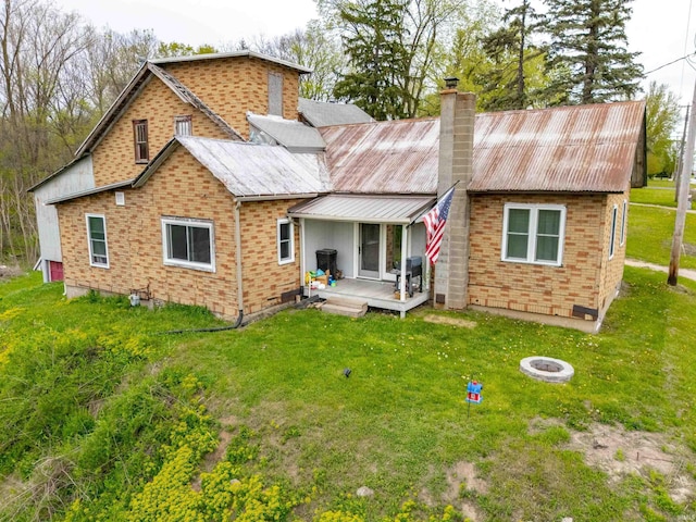 back of property with brick siding, an outdoor fire pit, a yard, and a chimney