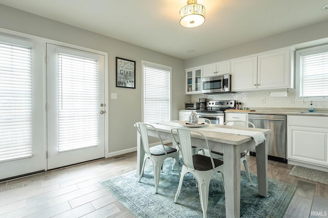 kitchen featuring tasteful backsplash, light wood-type flooring, white cabinets, glass insert cabinets, and stainless steel appliances