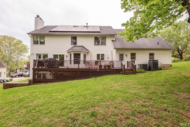 rear view of house featuring a deck, a chimney, central AC unit, roof mounted solar panels, and a yard
