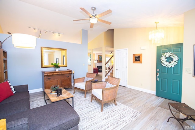 living room with light wood-style floors, rail lighting, ceiling fan with notable chandelier, stairs, and baseboards