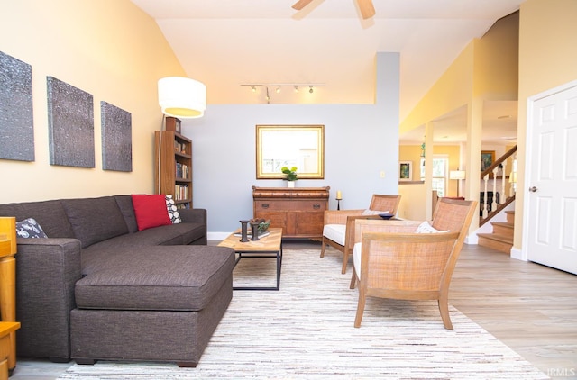 living area with a ceiling fan, stairway, track lighting, lofted ceiling, and light wood-style flooring