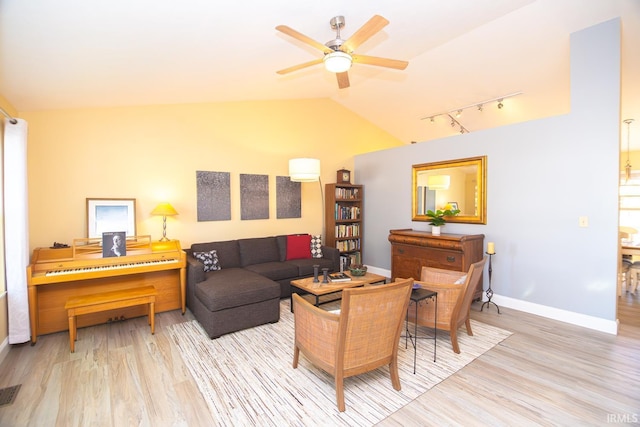 living area featuring wood finished floors, baseboards, ceiling fan, rail lighting, and vaulted ceiling
