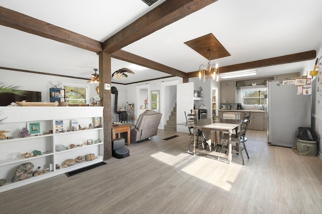 dining room with a wood stove, light wood-style flooring, stairs, and beamed ceiling