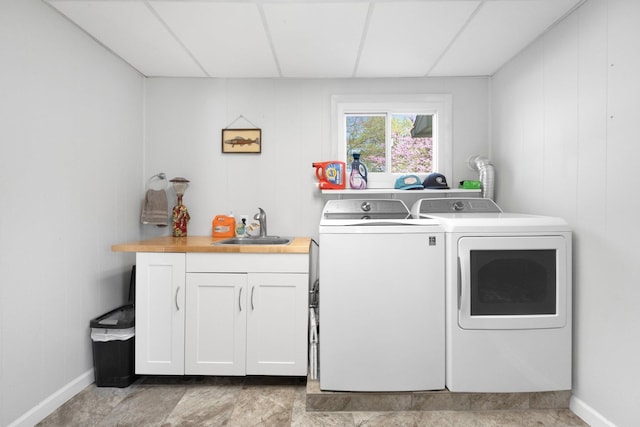 washroom featuring a sink, baseboards, cabinet space, and washer and dryer