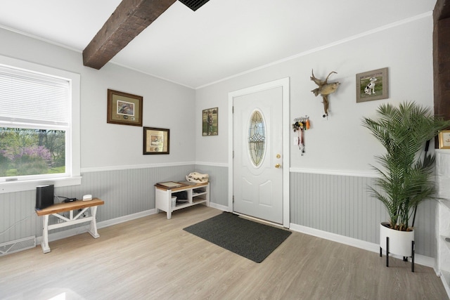 entryway with crown molding, beamed ceiling, wood finished floors, and a wainscoted wall