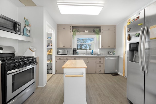 kitchen featuring appliances with stainless steel finishes, a sink, baseboards, light wood finished floors, and butcher block counters