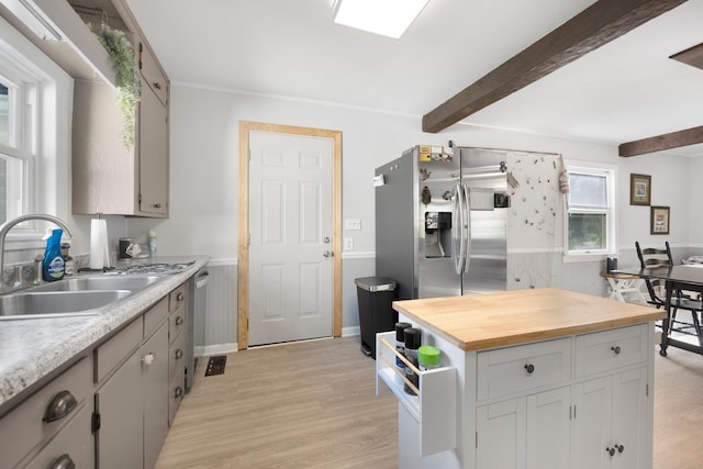 kitchen featuring beam ceiling, light wood-type flooring, a wainscoted wall, a sink, and stainless steel appliances
