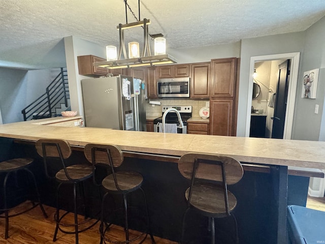 kitchen featuring brown cabinetry, a breakfast bar area, wood finished floors, light countertops, and stainless steel appliances
