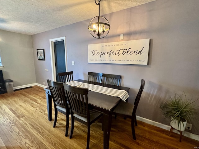 dining space with baseboards, a textured ceiling, wood finished floors, and a chandelier