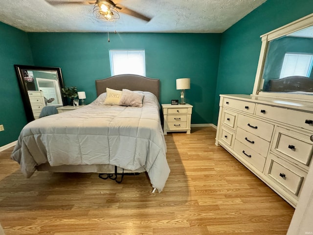 bedroom featuring a ceiling fan, a textured ceiling, baseboards, and light wood-type flooring