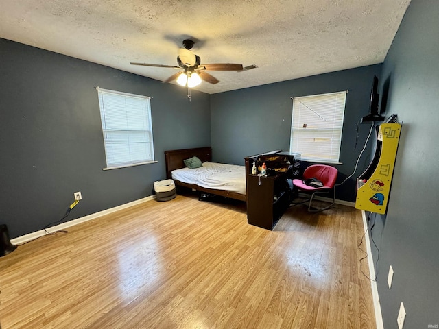 bedroom with a textured ceiling, a ceiling fan, baseboards, wood finished floors, and visible vents