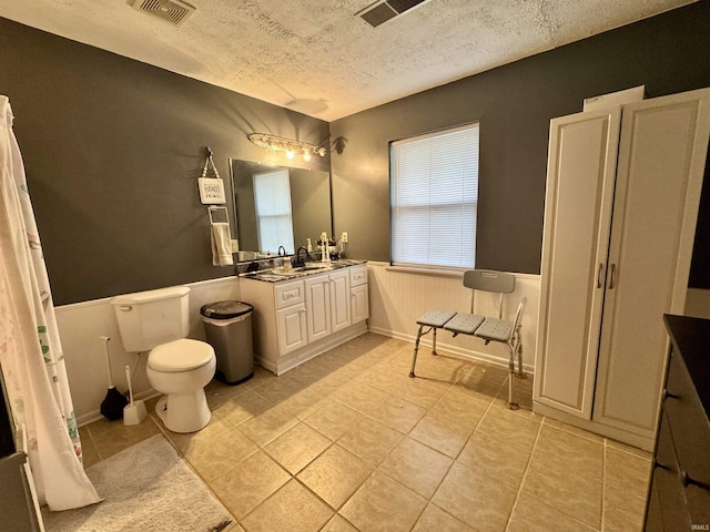bathroom with a textured ceiling, visible vents, tile patterned flooring, wainscoting, and vanity
