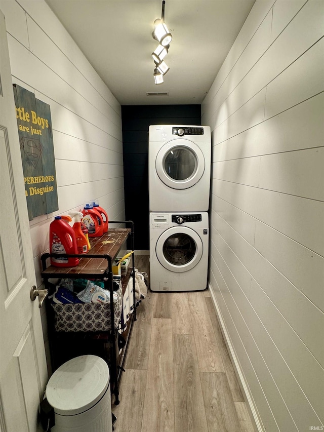 clothes washing area with stacked washing maching and dryer, light wood-style floors, wooden walls, and visible vents