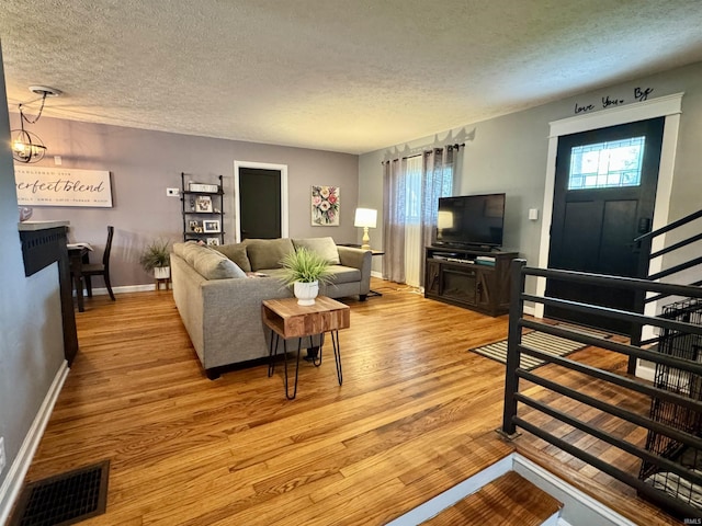 living area with light wood-style floors, baseboards, a textured ceiling, and visible vents