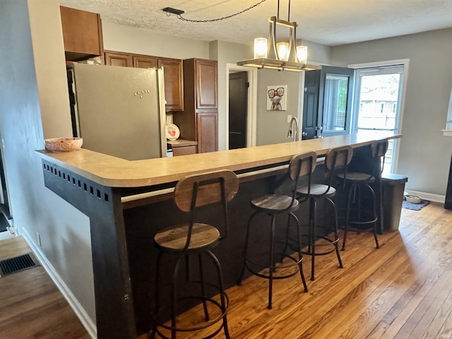 kitchen with visible vents, freestanding refrigerator, wood finished floors, light countertops, and hanging light fixtures