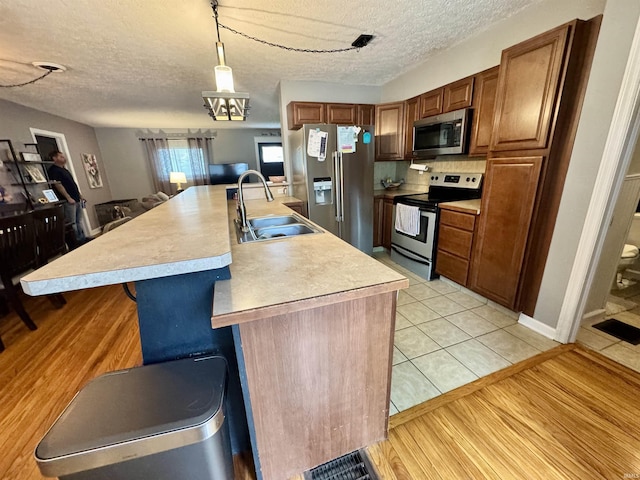 kitchen with a sink, light countertops, a textured ceiling, stainless steel appliances, and light tile patterned floors