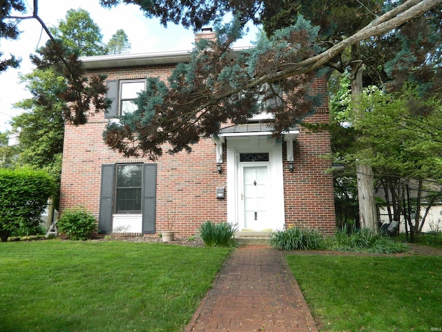 view of front of property featuring brick siding, a front lawn, and a chimney