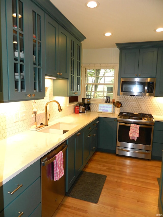 kitchen with light countertops, tasteful backsplash, a sink, light wood-style flooring, and appliances with stainless steel finishes