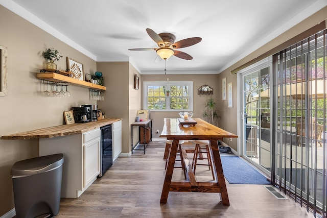 dining room featuring ceiling fan, a dry bar, wood finished floors, baseboards, and beverage cooler