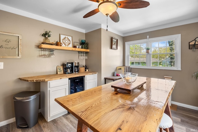 dining room featuring a bar, baseboards, wine cooler, and wood finished floors