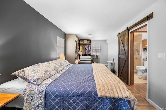 bedroom with ensuite bath, a barn door, wood finished floors, and a closet