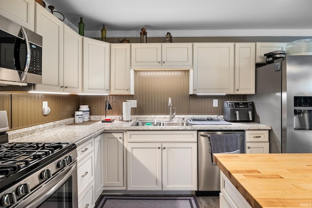 kitchen with a sink, white cabinets, stainless steel appliances, and butcher block counters