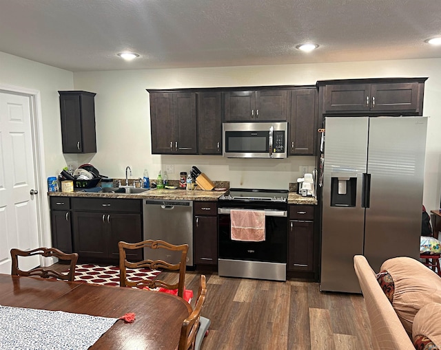 kitchen featuring light stone counters, a sink, dark wood-style floors, and stainless steel appliances