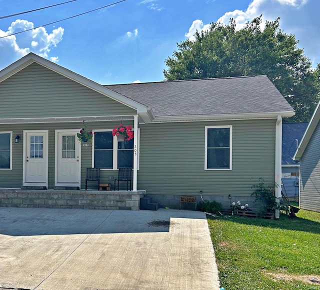 view of front of property with roof with shingles, covered porch, and a front lawn