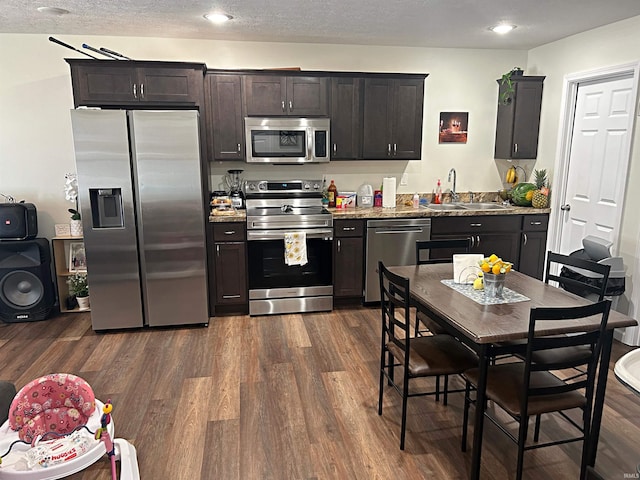 kitchen with appliances with stainless steel finishes, dark wood finished floors, a sink, light stone counters, and recessed lighting