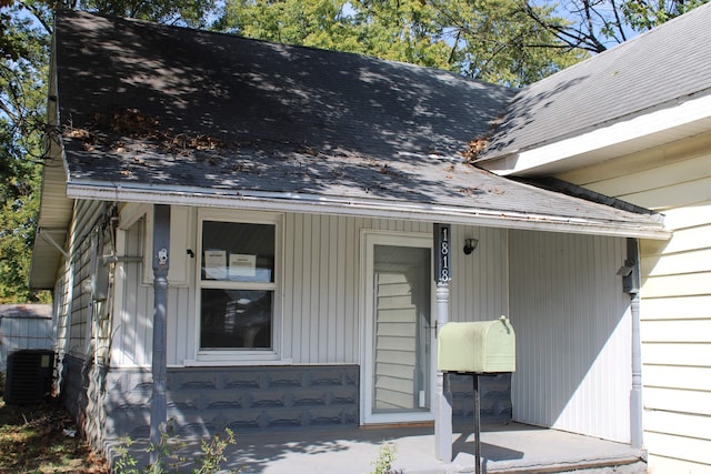entrance to property with central air condition unit, a shingled roof, and a porch
