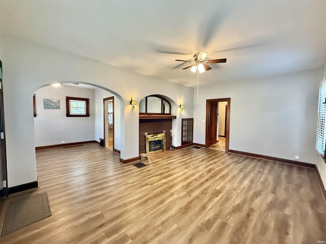 unfurnished living room featuring light wood-style floors, a brick fireplace, ceiling fan, and baseboards