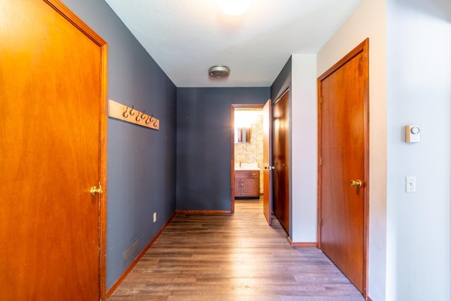 hall featuring baseboards, wood finished floors, and visible vents