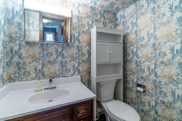 bathroom with toilet, wallpapered walls, and vanity