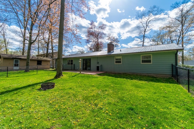 back of house with a lawn, metal roof, a chimney, and a fenced backyard
