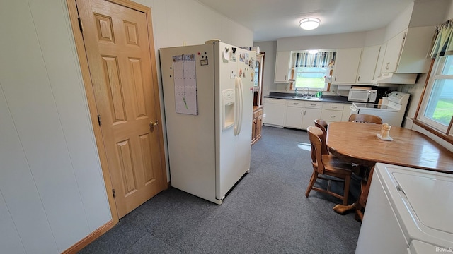 kitchen featuring white cabinets, dark countertops, a sink, white appliances, and washer / dryer