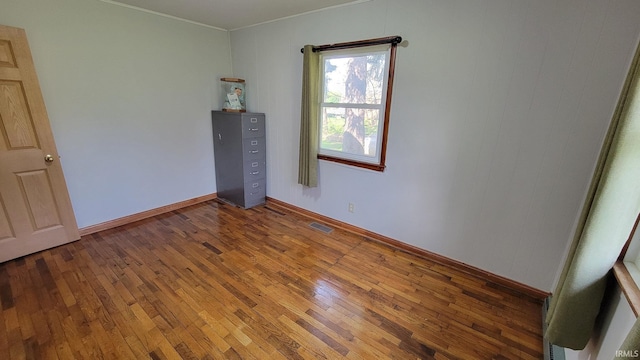 empty room featuring baseboards, ornamental molding, hardwood / wood-style floors, and visible vents