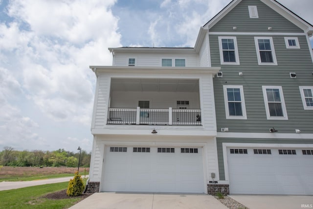 view of property with an attached garage, a balcony, and concrete driveway