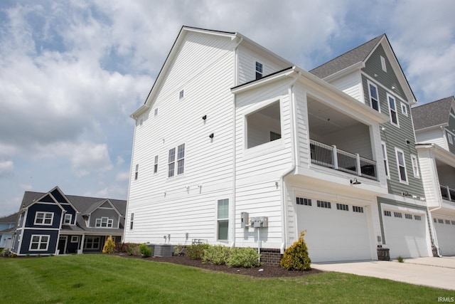 view of side of property featuring an attached garage, concrete driveway, cooling unit, a balcony, and a yard