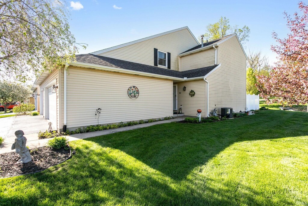 back of property featuring driveway, central air condition unit, a yard, an attached garage, and a shingled roof