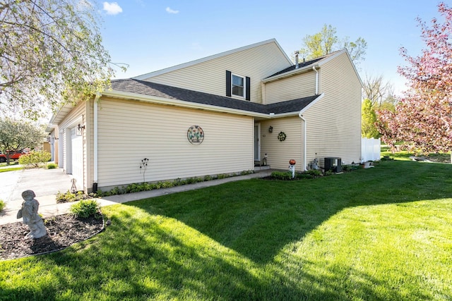 back of property featuring driveway, central air condition unit, a yard, an attached garage, and a shingled roof
