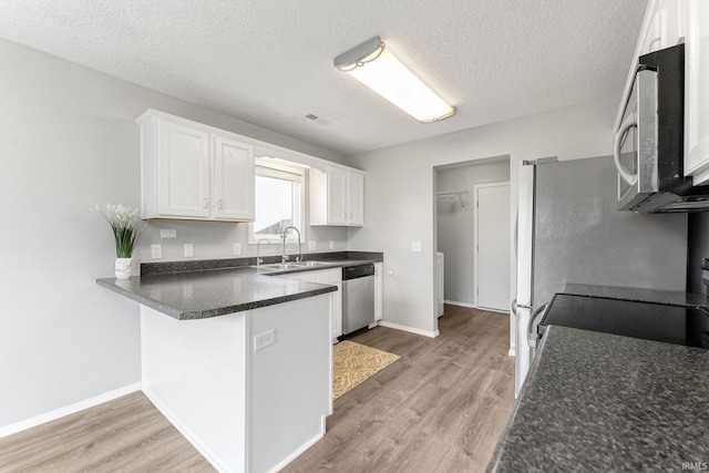 kitchen featuring white cabinets, stainless steel appliances, light wood-style flooring, and a peninsula