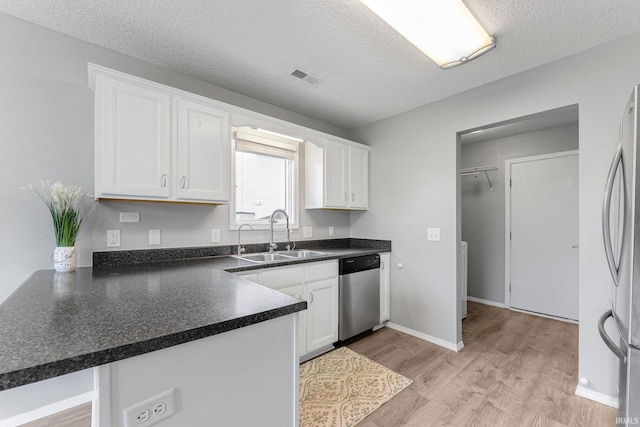 kitchen with white cabinets, appliances with stainless steel finishes, a sink, a peninsula, and light wood-type flooring