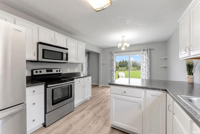kitchen with a peninsula, dark countertops, white cabinetry, a chandelier, and stainless steel appliances