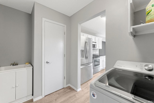 clothes washing area with laundry area, light wood-style floors, baseboards, washer / clothes dryer, and a sink