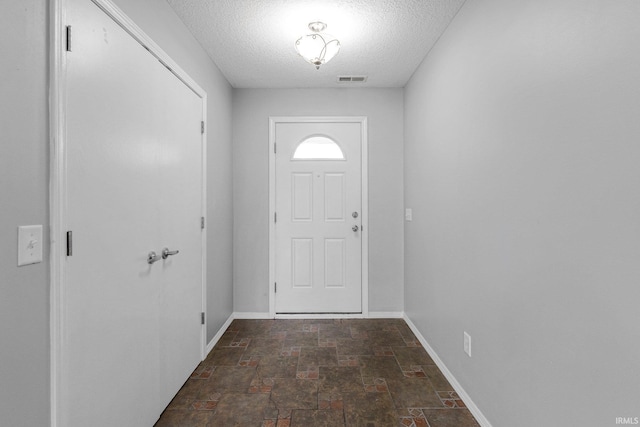doorway to outside with stone tile flooring, a textured ceiling, baseboards, and visible vents