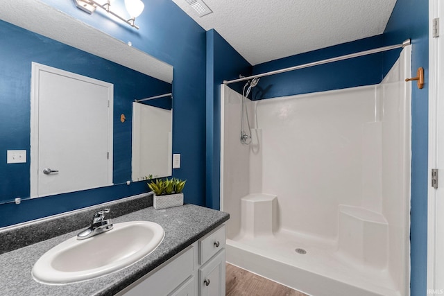 full bathroom featuring vanity, a shower stall, a textured ceiling, and wood finished floors